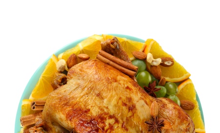 whole roasted chicken with grapes, oranges and spices on blue plate on white background close-upの写真素材