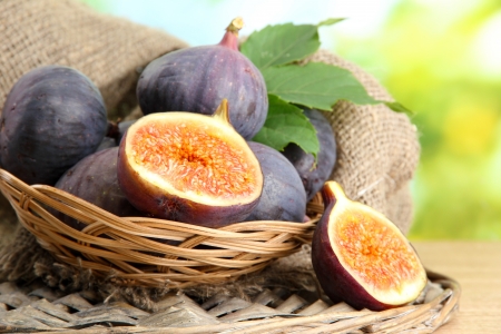 Ripe sweet figs with leaves in basket, on wooden table, on green backgroundの写真素材