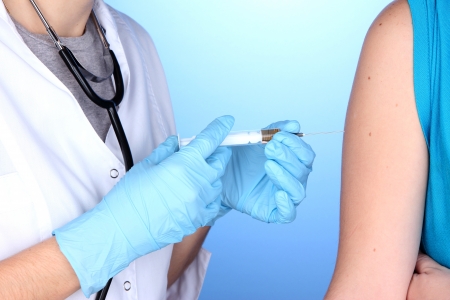doctor holding syringe with vaccine into patient's shoulder on blue backgroundの写真素材