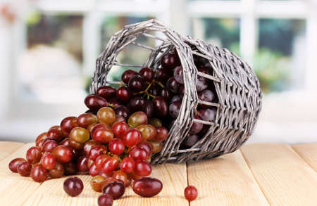 Ripe pink grapes in basket on wooden table on window backgroundの写真素材