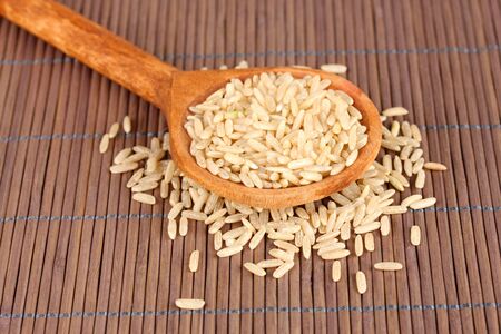 rice  in wooden  spoon on bamboo matの写真素材