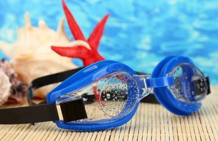 blue swim goggles with drops on a bamboo pad, on blue sea backgroundの写真素材