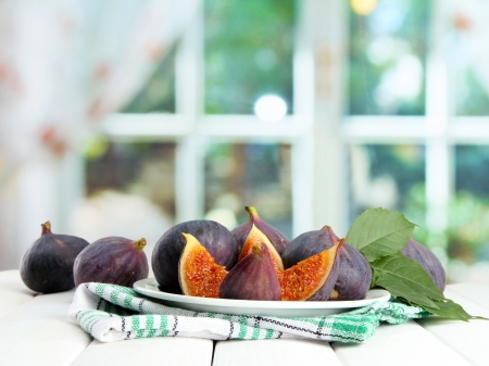 Ripe sweet figs with leaves on plate, on wooden table, on window backgroundの写真素材