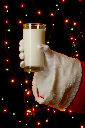 Santa Claus hand holding glass of milk on bright backgroundの写真素材