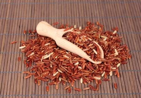 red rice  in wooden  scoop on bamboo matの写真素材