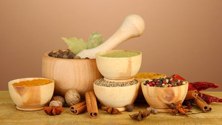 mortar, bowls and spoons with spices, on table on brown backgroundの写真素材
