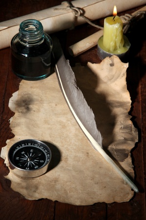 Old paper with ink pen near lighting candle on wooden table