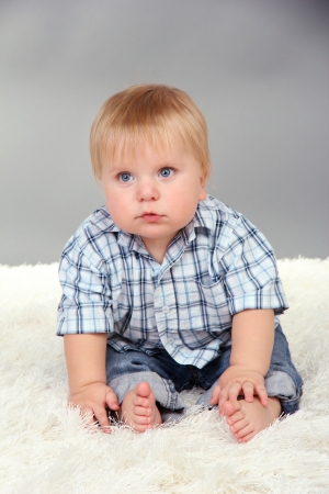 Little boy sitting on white carpet on gray backgroundの写真素材