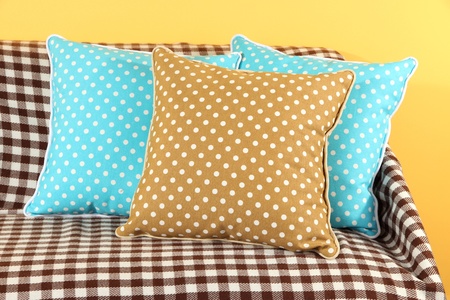 Colorful pillows on couch on yellow background