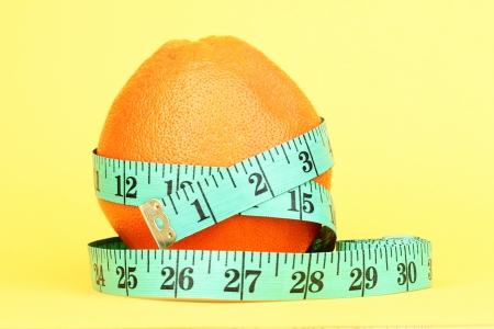orange with measuring tape on yellow backgroundの写真素材