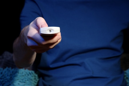Man hand holding a TV remote control, on dark backgroundの写真素材