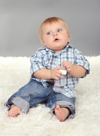 Little boy sitting on white carpet on gray backgroundの写真素材