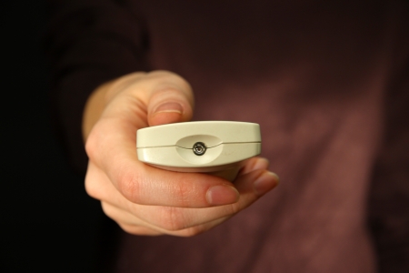 Woman hand holding a TV remote control, on dark backgroundの写真素材