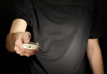 Man hand holding a TV remote control, on dark backgroundの写真素材