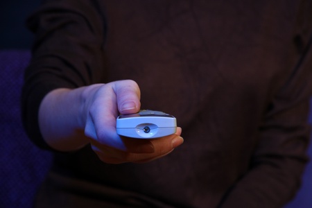 Woman hand holding a TV remote control, on dark backgroundの写真素材