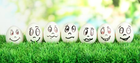 Eggs with funny faces on grass on bright backgroundの写真素材