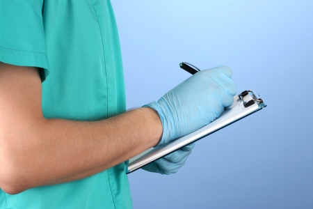 Hand of doctor with pen writing on prescription blank, on blue backgroundの写真素材