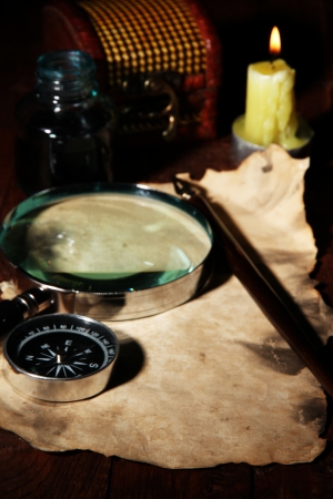 Old paper with ink pen and magnifying glass near lighting candle on wooden tableの写真素材