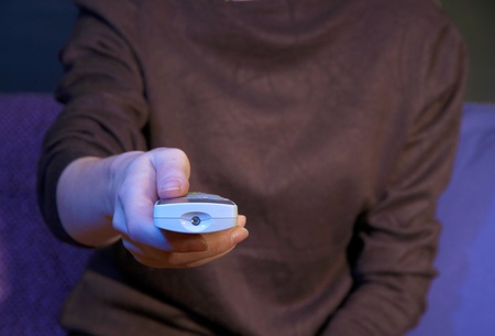 Woman hand holding a TV remote control, on dark background
