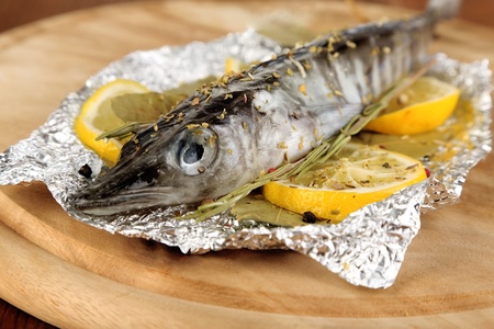Fish in foil with herbs and lemon on board on wooden table close-upの写真素材
