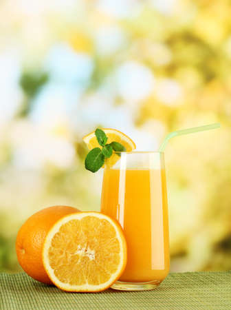 Glass of orange juice with mint and orange on table on bright backgroundの写真素材