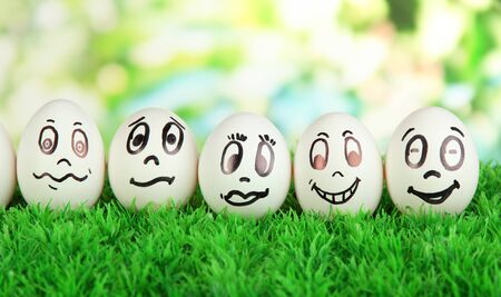 Eggs with funny faces on grass on bright backgroundの写真素材