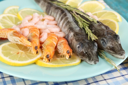 Fresh fishes with shrimp and lemon on plate on wooden table close-up