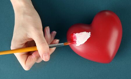 Hand paints white spot on heart, on color background. Conceptual photo treatment of heart disease.の写真素材