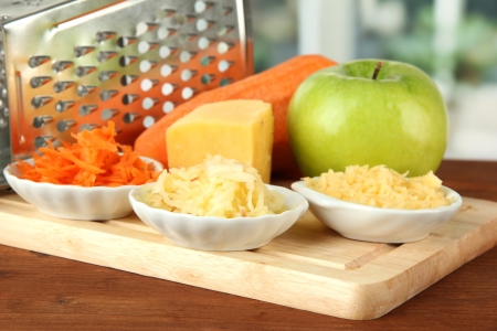 Metal grater and apple, cheese, carrot, on cutting board, on bright backgroundの写真素材