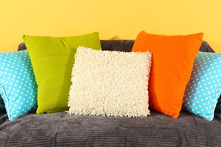 Colorful pillows on couch on yellow background
