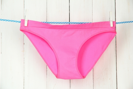 Womans panties hanging on a clothesline, on white wooden background