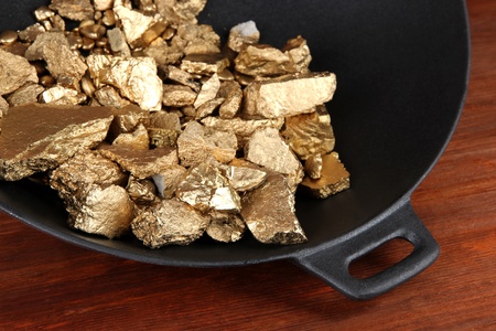Gold pan with golden nuggets inside on wooden backgroundの写真素材