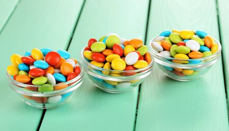 Colorful candies in glass bowls on green wooden background