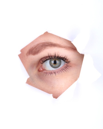 Female eye looking through hole in sheet of paperの写真素材