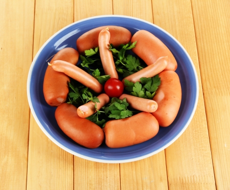Sausage, greens, tomato on plate on wooden tableの写真素材