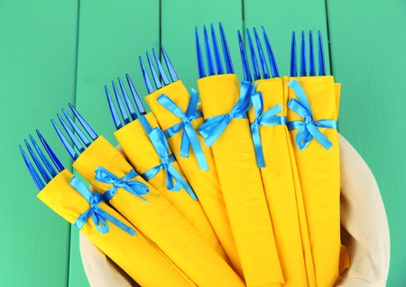 Blue plastic forks wrapped in yellow paper napkins, in basket, on color wooden backgroundの写真素材
