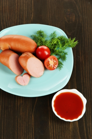 Sausage, greens, tomato on plate on wooden tableの写真素材