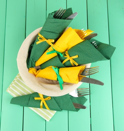 Forks and knives wrapped in green and yellow paper napkins, on color wooden backgroundの写真素材