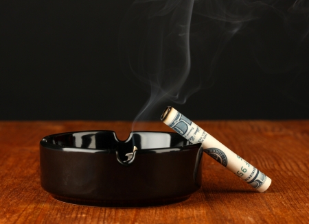 smoking cigarette of the 100 dollar bill and an ashtray on black backgroundの写真素材