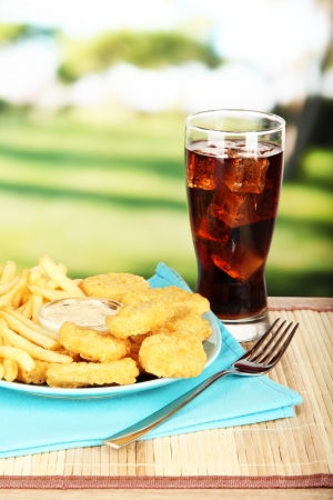 Fried chicken nuggets with french fries,cola and sauce on table in parkの写真素材