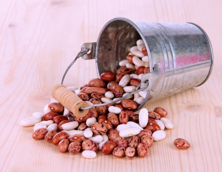 Overturned bucket with beans on wooden background