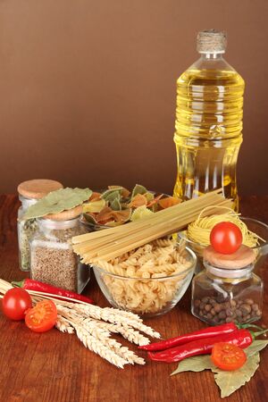 Different types of pasta, spices, tomatoes on a wooden table on brown backgroundの写真素材