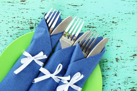 Forks and knives wrapped in blue paper napkins, on color wooden backgroundの写真素材