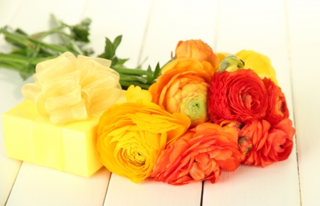 Ranunculus (persian buttercups) and gift, on white wooden background