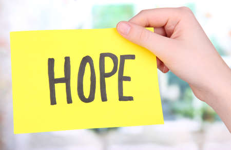 Hope word on piece paper in hand on window backgroundの写真素材