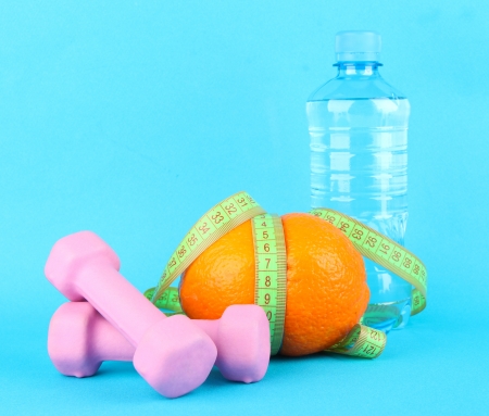 Orange with measuring tape, dumbbells and bottle of water, on color backgroundの写真素材