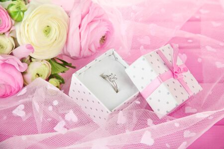 Ranunculus (persian buttercups) and engagement ring, on pink cloth