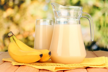 Full glass and jug of banana juice and bananas on wooden table outdoorの写真素材