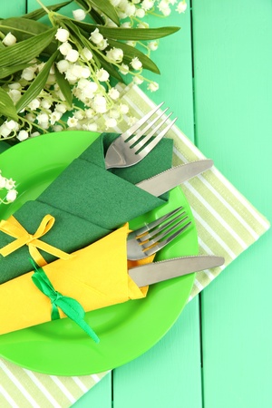 Forks and knives wrapped in green and yellow paper napkins, on color wooden backgroundの写真素材