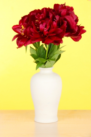 Beautiful peonies in vase on table on yellow backgroundの写真素材